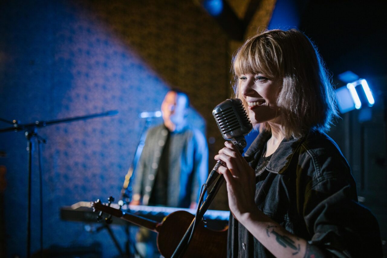 Smiling caucasian woman singing with vintage microphone during live music performance.